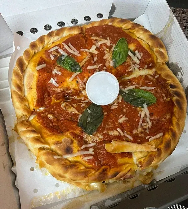 Pizza topped with basil and grated cheese in a takeaway box