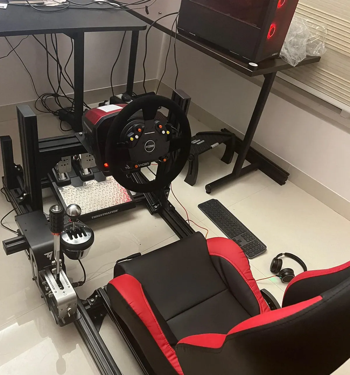 Sim racing rig with a wheel, pedals and a red bucket seat