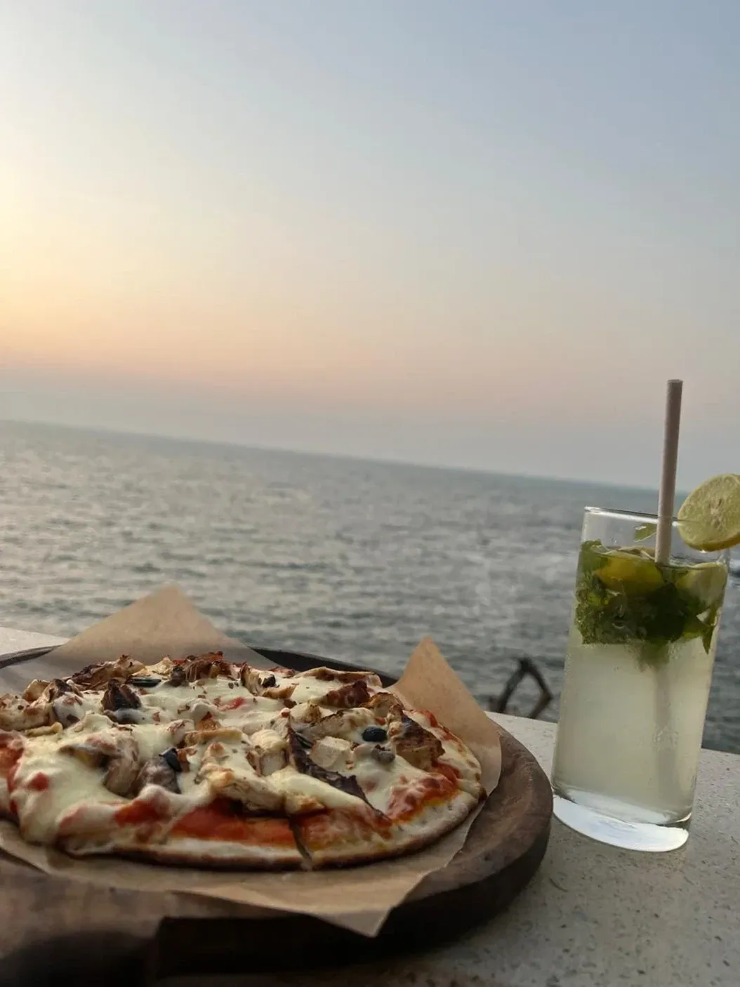 Pizza and a mojito on a table by the sea at sunset