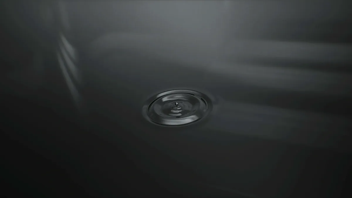 Chrome drop rippling on a dark liquid surface